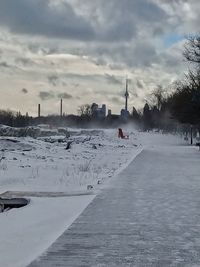 Snow covered road by city against sky