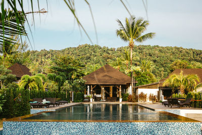 Swimming pool outside villa by green trees against sky at resort