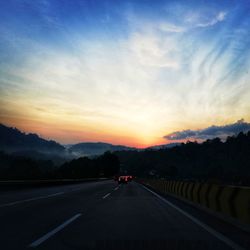 Cars on highway against sky during sunset
