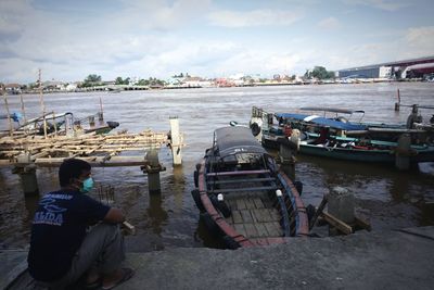 Rear view of people sitting on shore against sky