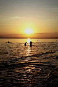 Silhouette people on sea against sky during sunset