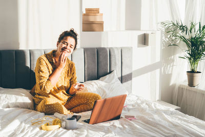 Young woman using laptop while sitting on bed at home