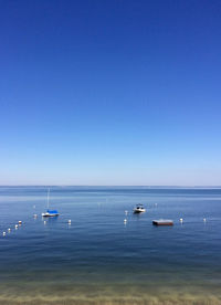 Boats in calm sea against clear sky