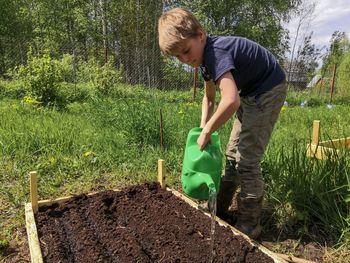 The boy waters the garden from a watering can.