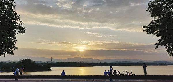 People on lake against sky during sunset