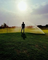 Man standing by sprinklers on grassy field against sky
