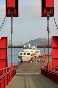 Small ferry at port on sea against sky and mountain