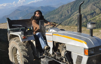 A south asian long haired man looking at camera while driving an old tractor in hilly area