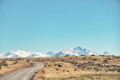 Road leading towards mountains against clear blue sky