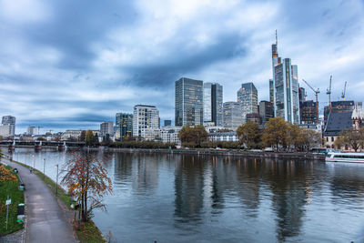 Buildings by river against cloudy sky