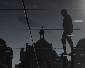 Low angle view of silhouette man standing by building against sky