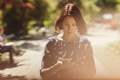 Businesswoman using smart phone on footpath in park during summer