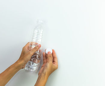 Close-up of hand holding bottle against white background