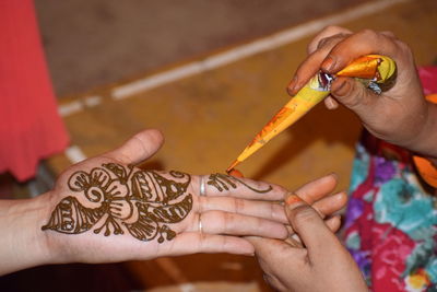Cropped image of woman applying henna tattoo on friend hand