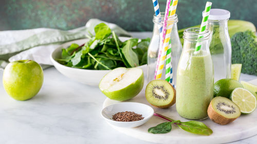 A bottle of green smoothie surrounded by ingredients used to make it.