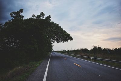 Empty road by trees against sky