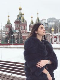 Woman in warm clothing standing against buildings during winter