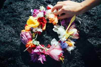 Hawaiian flower lei on lava rocks with one hand in kauai, hawaii.