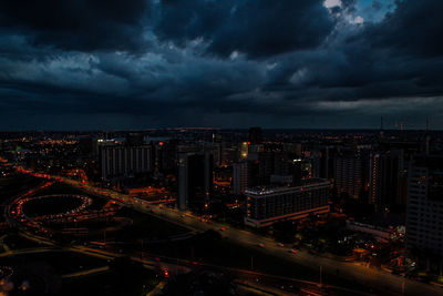Aerial view of city lit up against cloudy sky