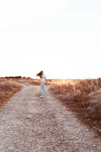 Rear view of man walking on street amidst field against clear sky