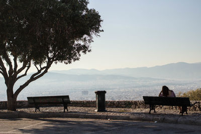 Rear view of man sitting on bench by lake against clear sky