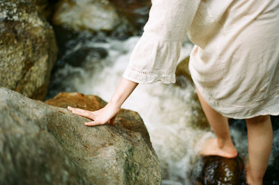 Low section of woman on rock by stream