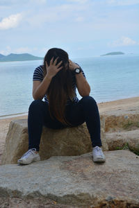 Young woman sitting on shore against sea