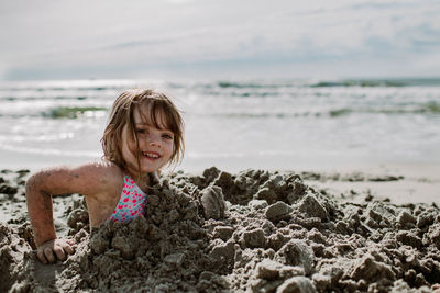 Young girl buried in the sand smiling at the beach