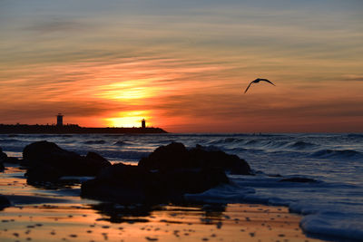 Silhouette rocks on beach against sky during sunset