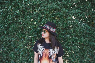 Woman in hat and sunglasses standing against plants