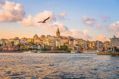 Buildings by river against sky during sunset