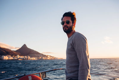 Man wearing sunglasses standing by sea against sky during sunset