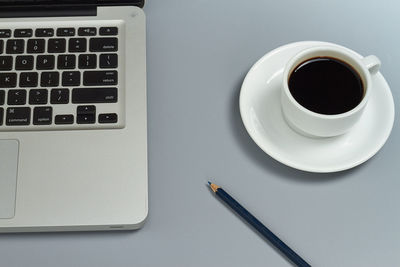 Close-up of coffee cup by laptop on table