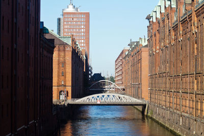 Bridge amidst building over canal against clear sky at speicherstadt