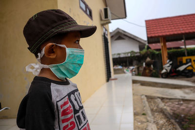 Side view of boy wearing pollution mask while standing on sidewalk