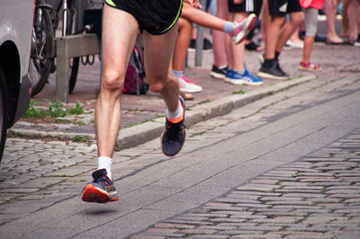 Low section of athlete running marathon on street with people in background