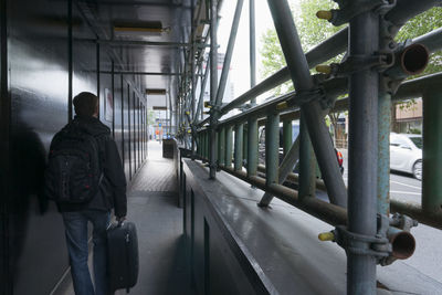 Rear view of man with luggage walking in passage by street