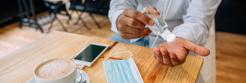 Midsection of man using hand sanitizer at cafe