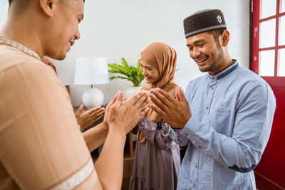 Rear view of couple greeting guest at home