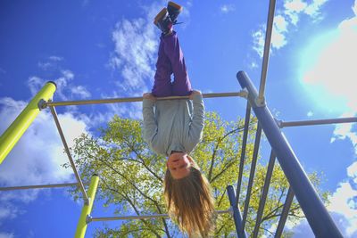 Beautiful blond girl with long hair playing in playground. young girl hanging upside down in a park.