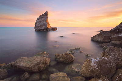 Rocks on sea against sky during sunset