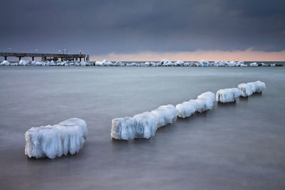 Frozen wooden posts on sea against cloudy sky