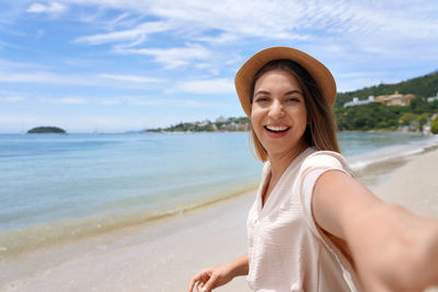 Portrait of young woman standing at beach against sky