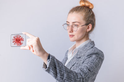 Portrait of young woman holding eyeglasses against white background