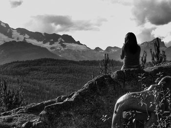 Rear view of woman sitting on mountain against sky