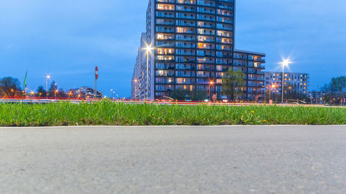 Surface level of road by illuminated buildings against sky