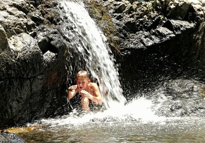 Boy enjoying in waterfall at forest