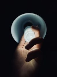 Close-up of hand holding light bulb against black background