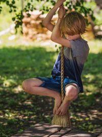 Rear view of boy swinging on rope in park