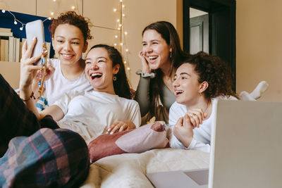 Cheerful multiracial female friends video calling through smart phone at home